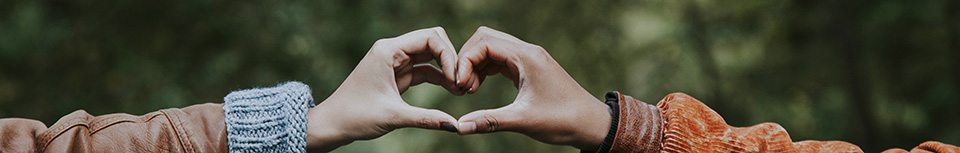 two people whose hands are forming the shape of a heart with trees in the background